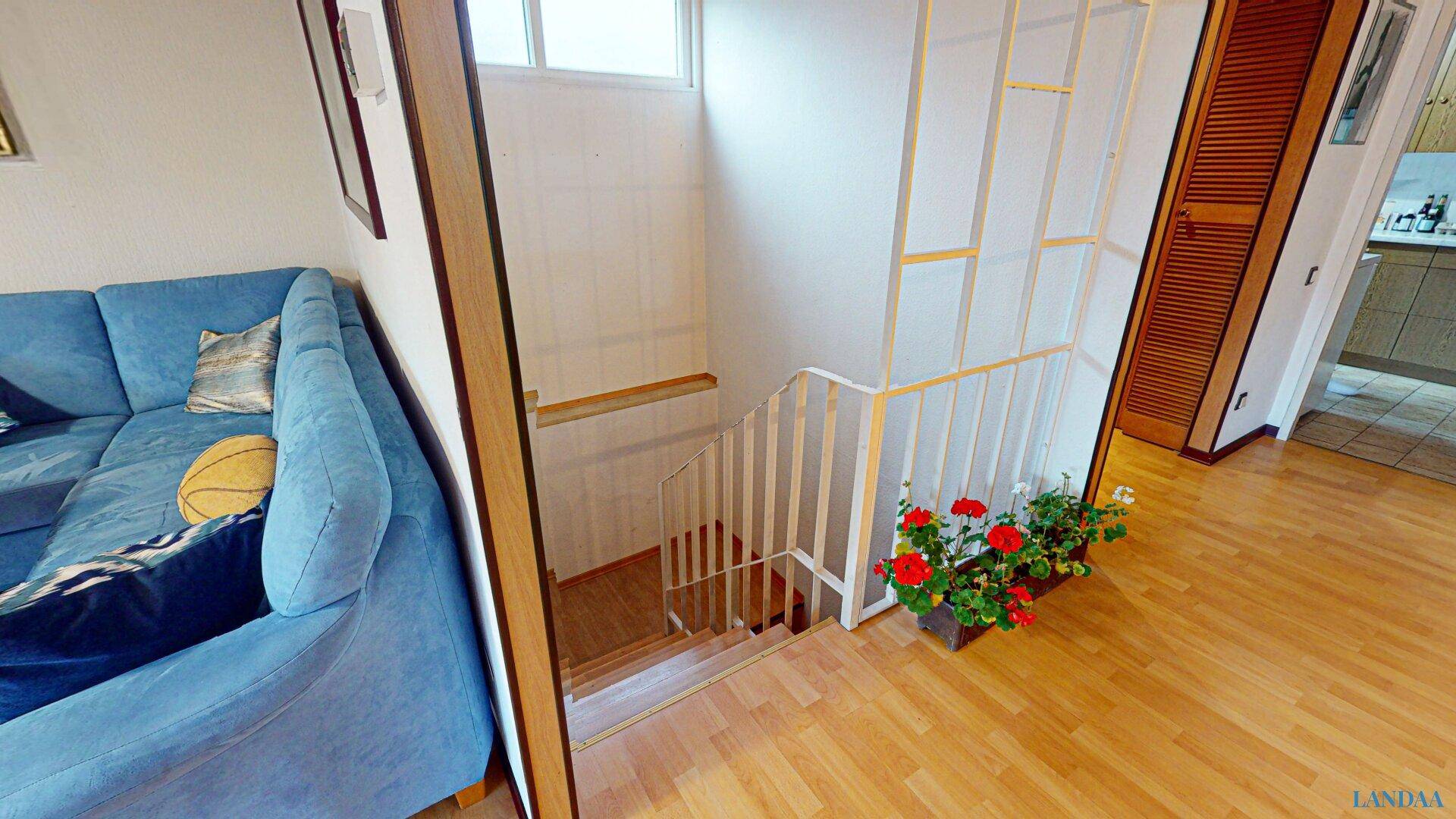 Wohnbereich mit blauem Sofa, Holzparkett und Treppe, die in eine andere Etage führt.