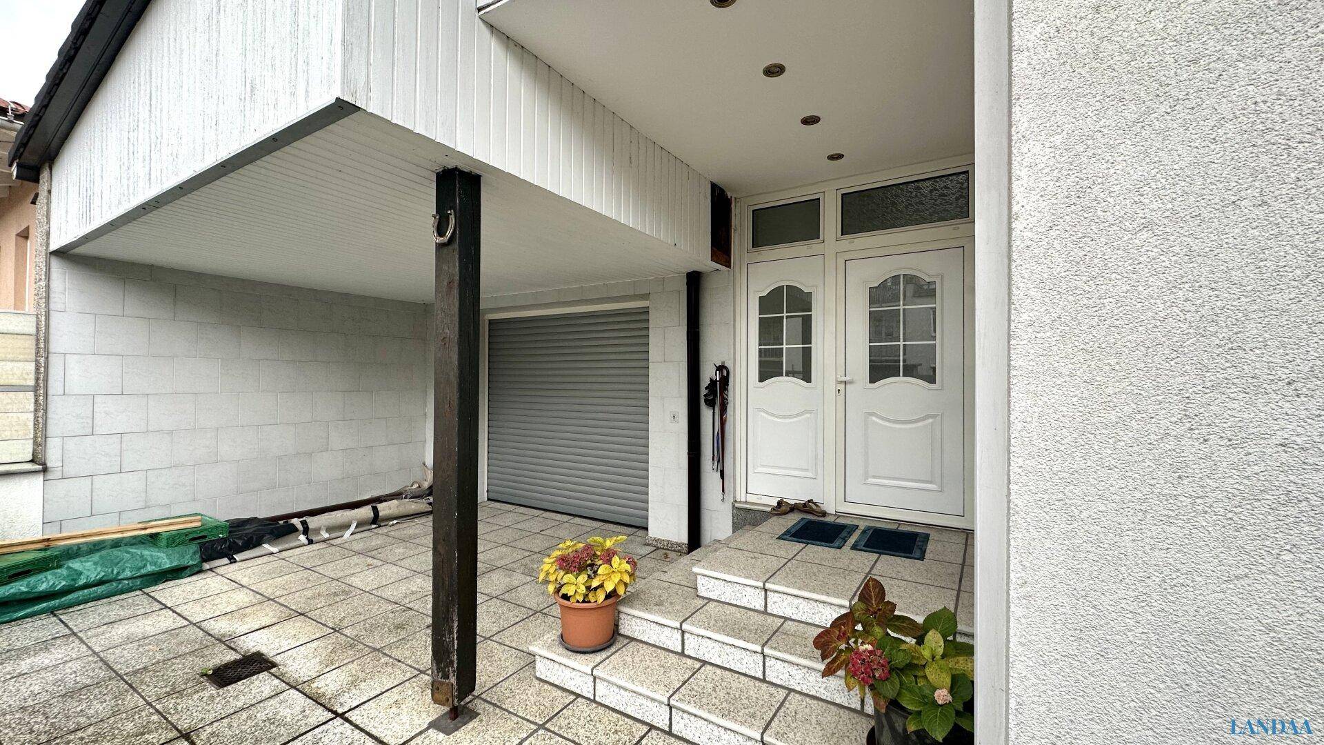 Eingangsbereich des Hauses mit Doppelhaustür, Garage und überdachtem Stellplatz.