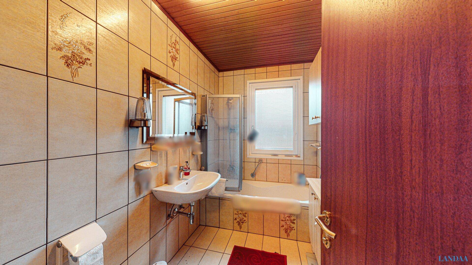 Badezimmer mit beigefarbenen Fliesen, Badewanne mit Duschabtrennung und Fenster.