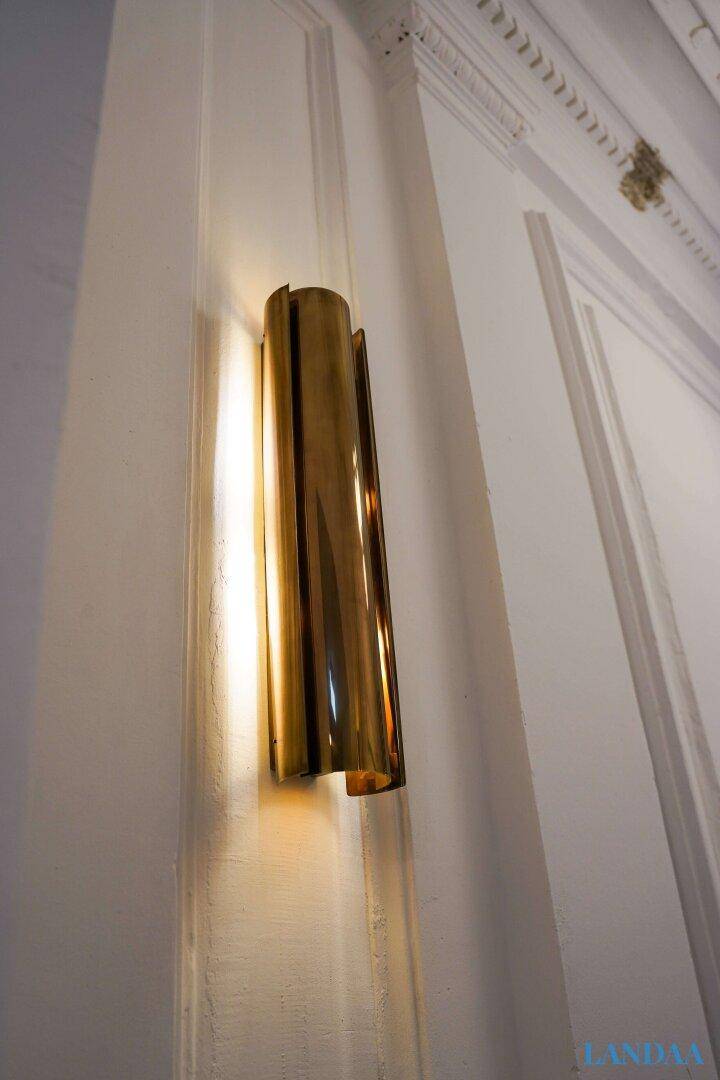 Elegante goldene Wandleuchte an einer weißen Wand mit feinen Stuckverzierungen an der Decke.