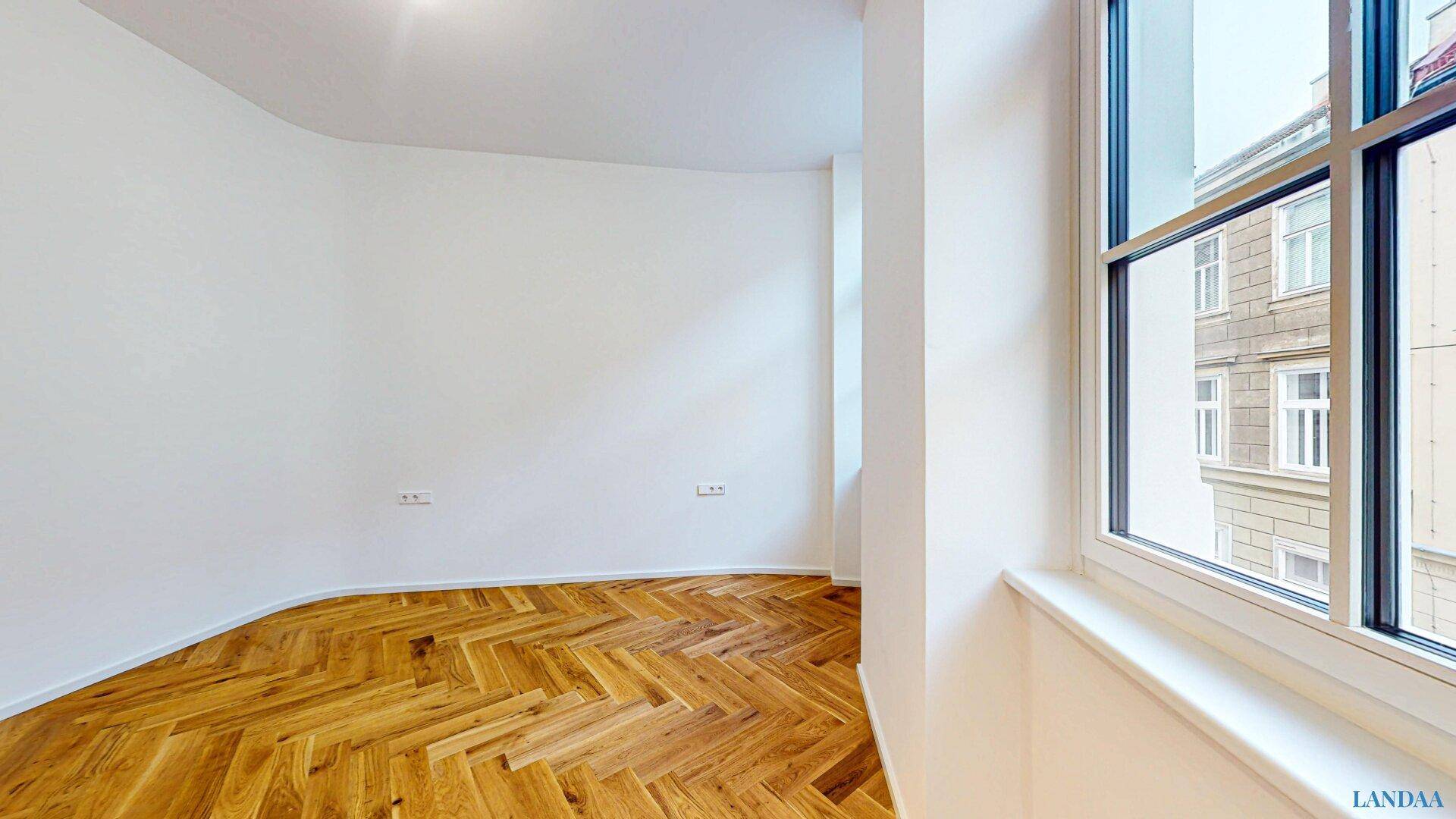 Lichtdurchfluteter Raum mit klassischem Fischgrätparkett und Blick auf die gegenüberliegende Architektur.