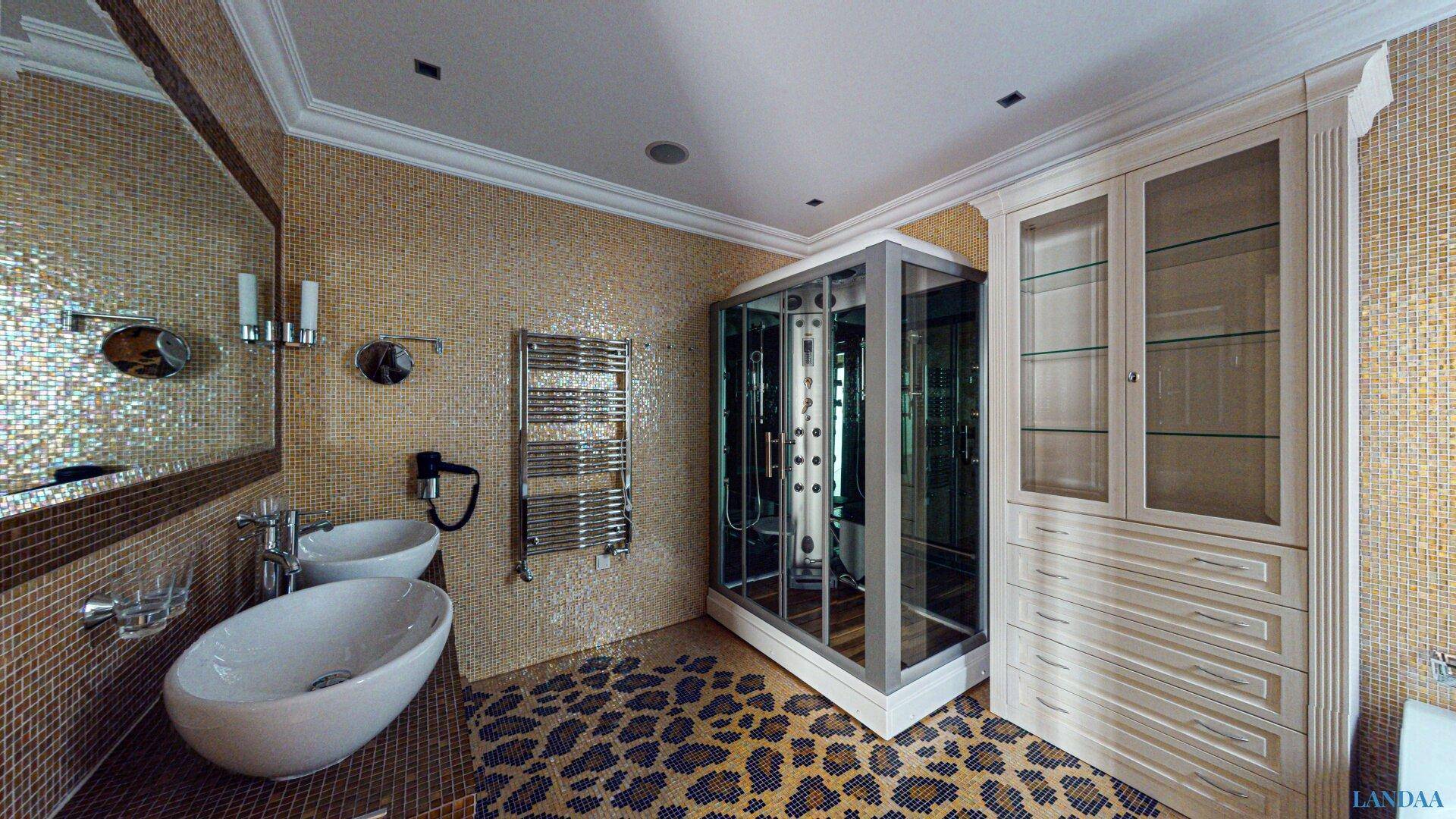 Luxuriöses Badezimmer mit goldenen Mosaikfliesen, Doppelwaschbecken und moderner Duschkabine.