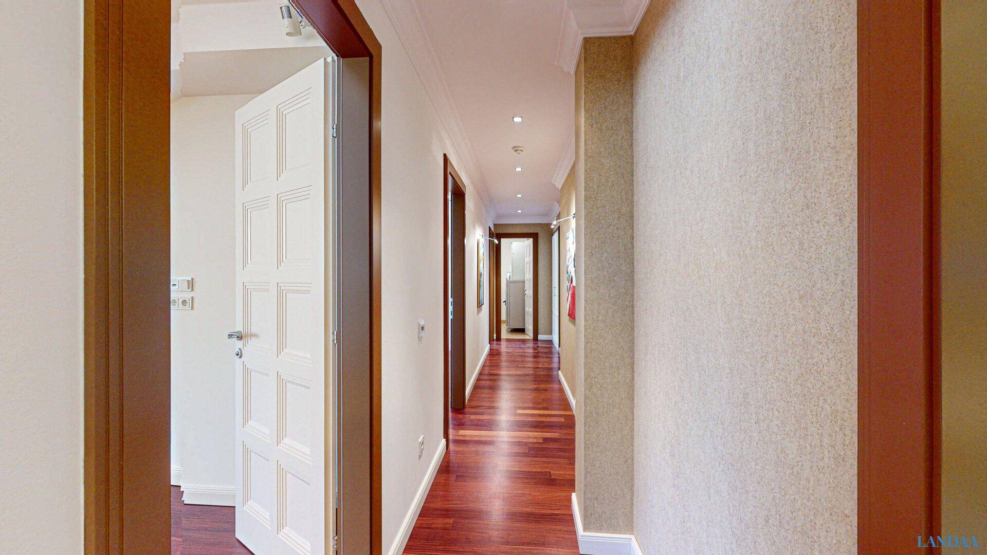 Langer Flur mit elegantem Holzfußboden und integrierter Deckenbeleuchtung.