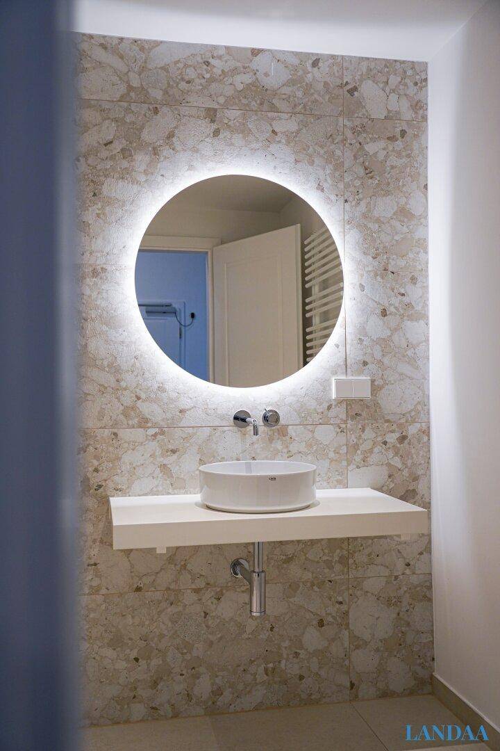 Modernes Badezimmer mit beleuchtetem Spiegel, Aufsatzwaschbecken und Marmorfliesen.