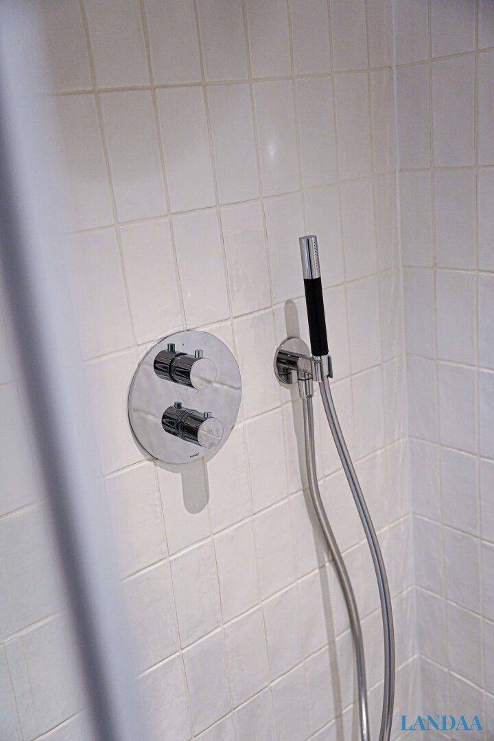 Moderne Duscharmaturen und Handbrause an weiß gefliesten Wänden in der Dusche.