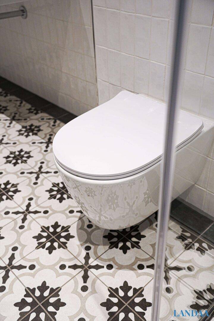 Detailaufnahme der gemusterten Bodenfliesen und des wandhängenden WCs im Badezimmer.