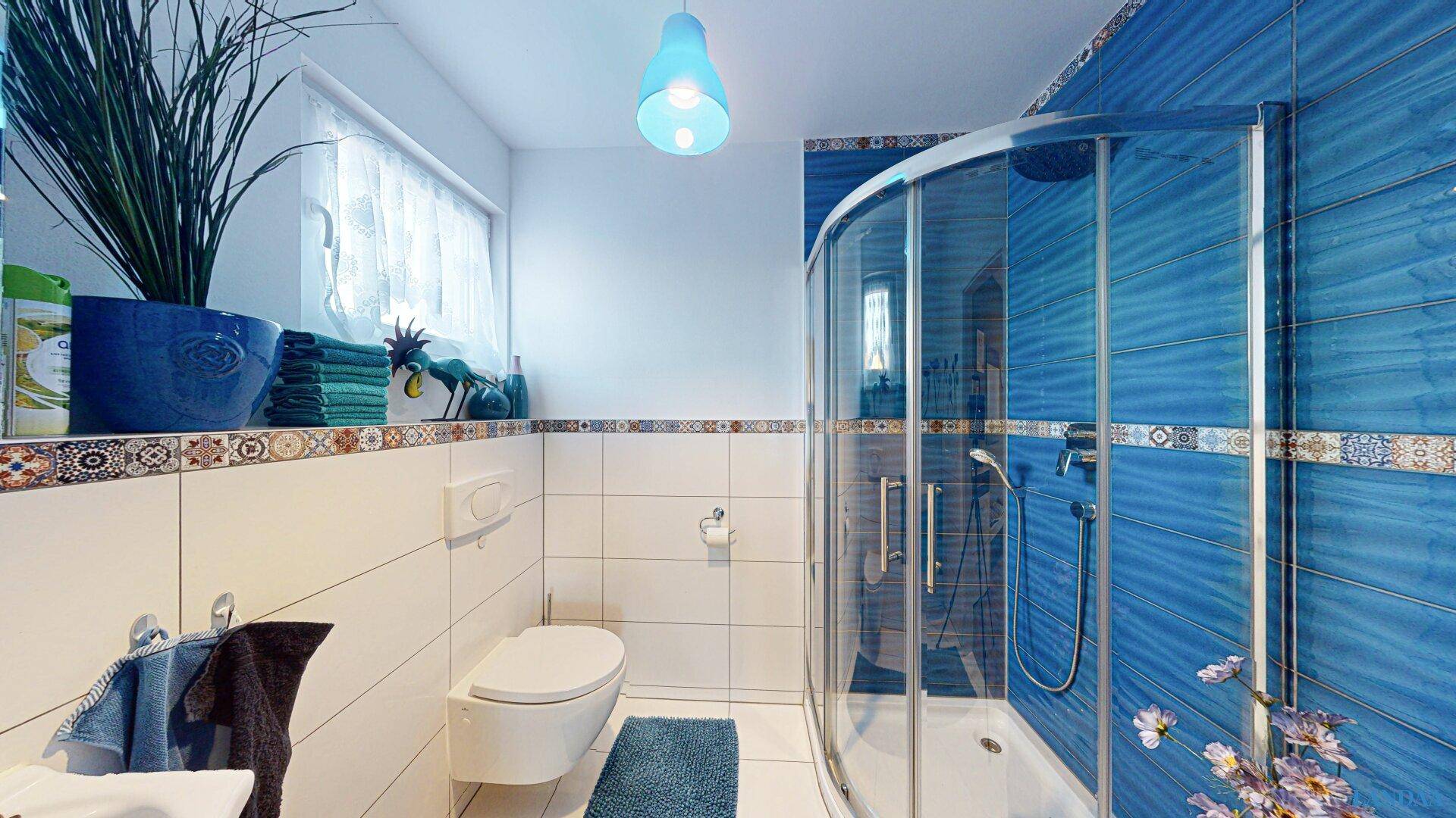Modernes Badezimmer mit Duschkabine, blauen Fliesen und Fenster.