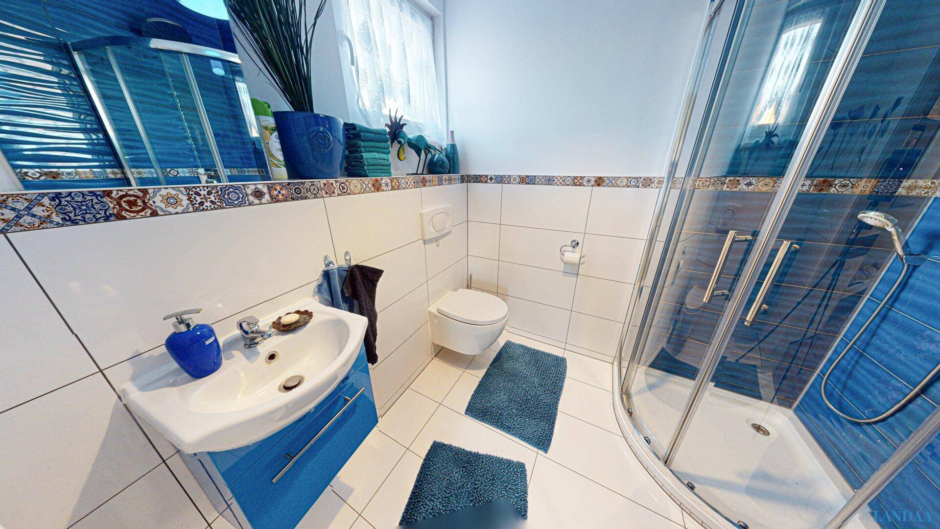 Helles Badezimmer mit Duschkabine, Waschbecken und blauen Akzenten.