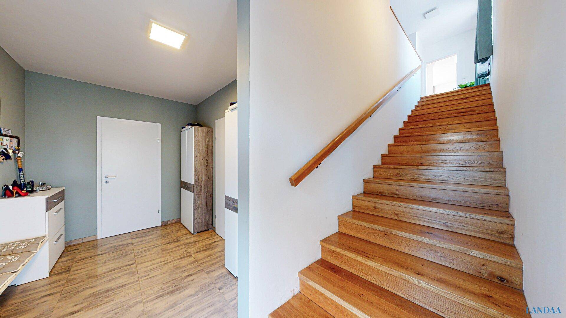 Geräumiger Flur mit Holztreppe und Fliesenboden, der zu den oberen Etagen führt.