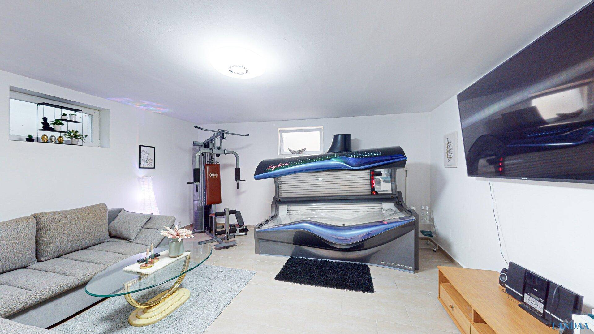 Geräumiger Kellerraum mit Fitnessgeräten, Solarium und Fernseher.