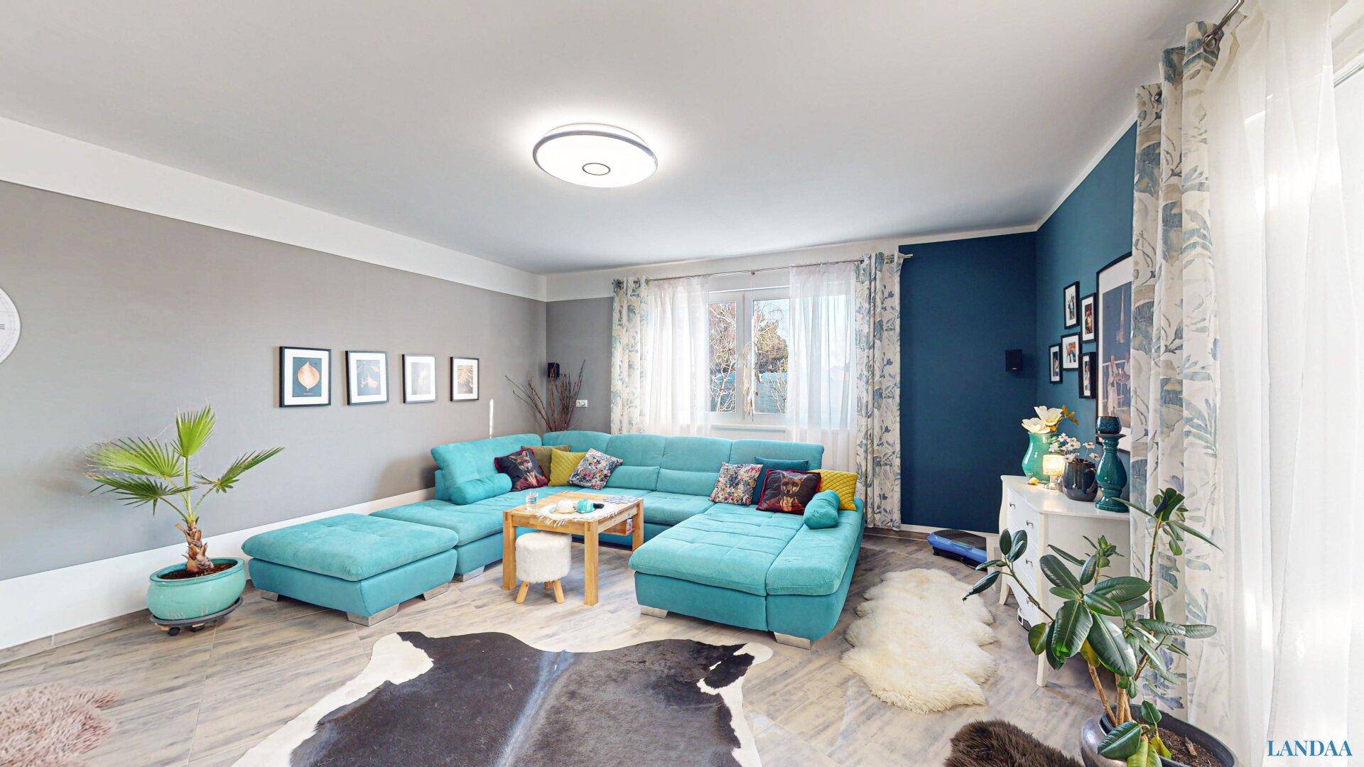 Helles Wohnzimmer mit türkisfarbenem Ecksofa, Kuhfellteppich und modernem Dekor.