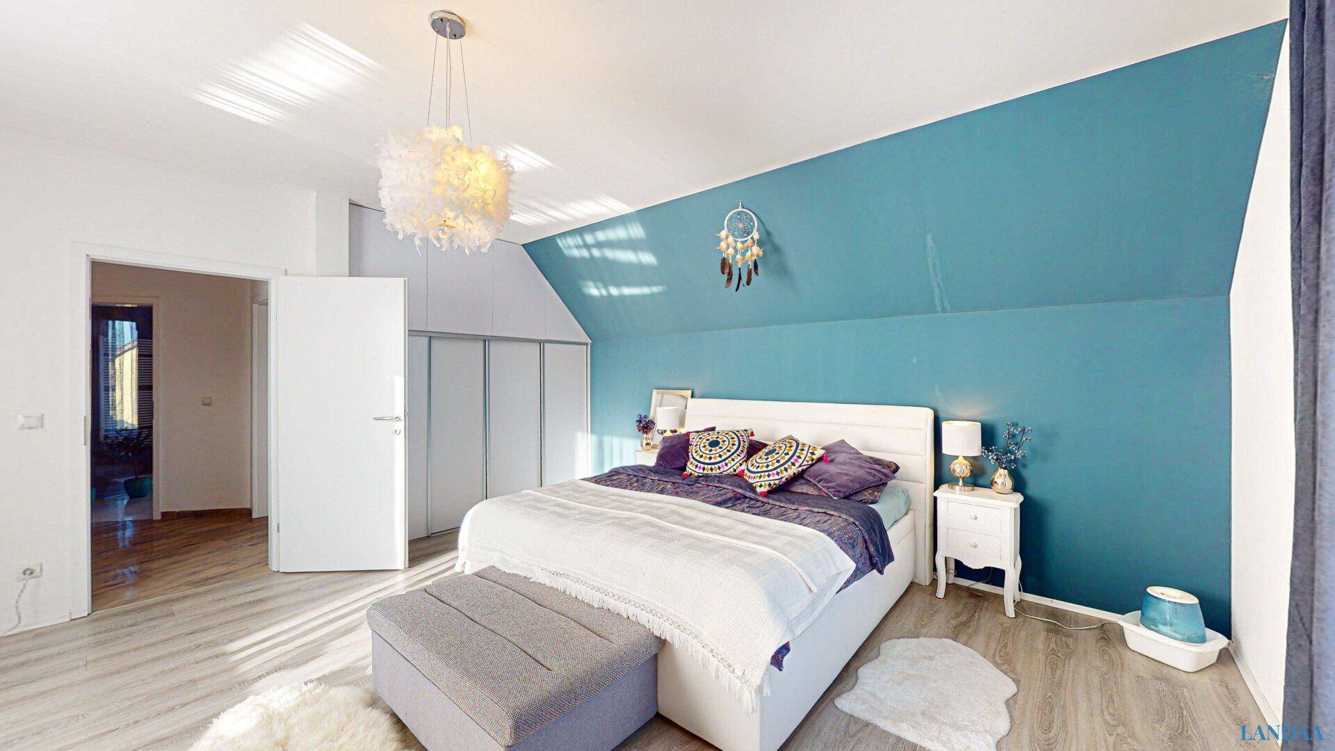 Gemütliches Schlafzimmer mit Doppelbett, Dachschräge und blauer Akzentwand.