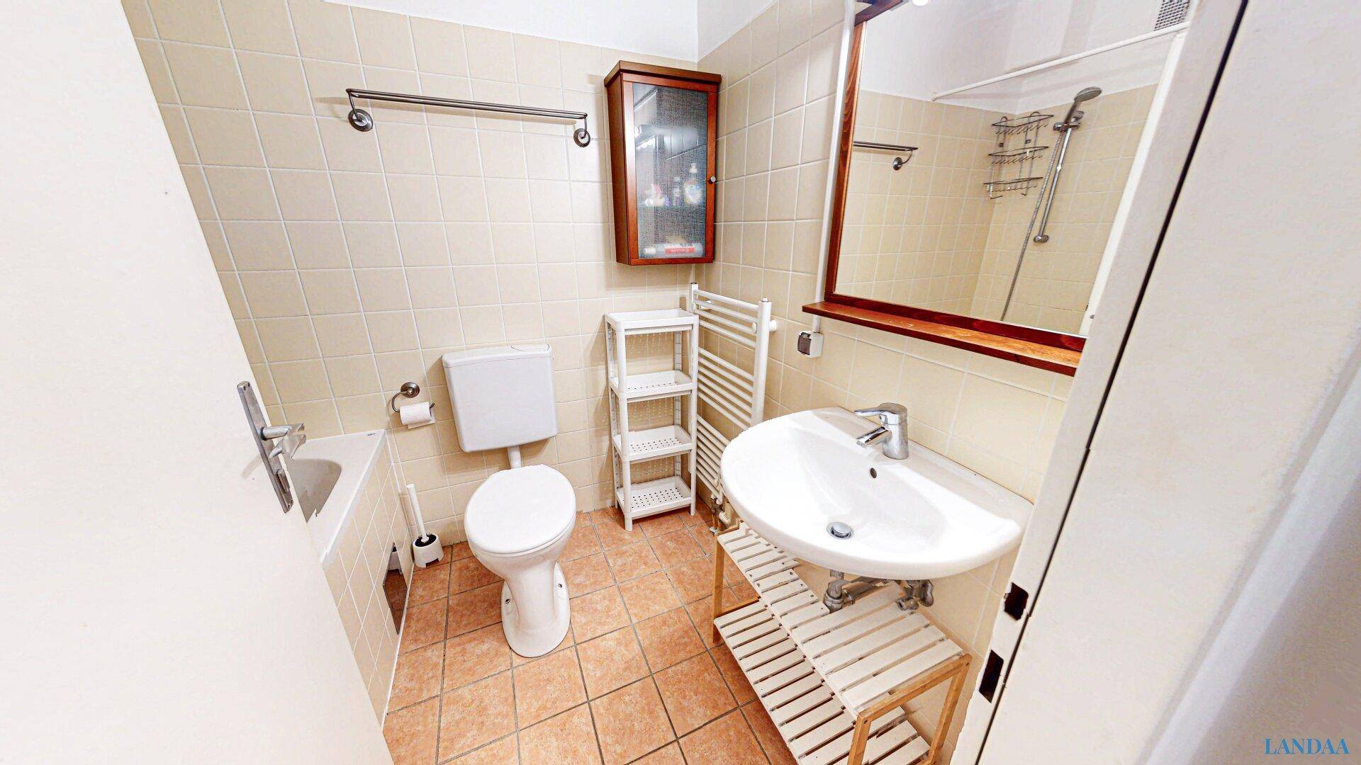 Badezimmer mit beigefarbenen Fliesen, Waschbecken, Toilette und Handtuchheizkörper.
