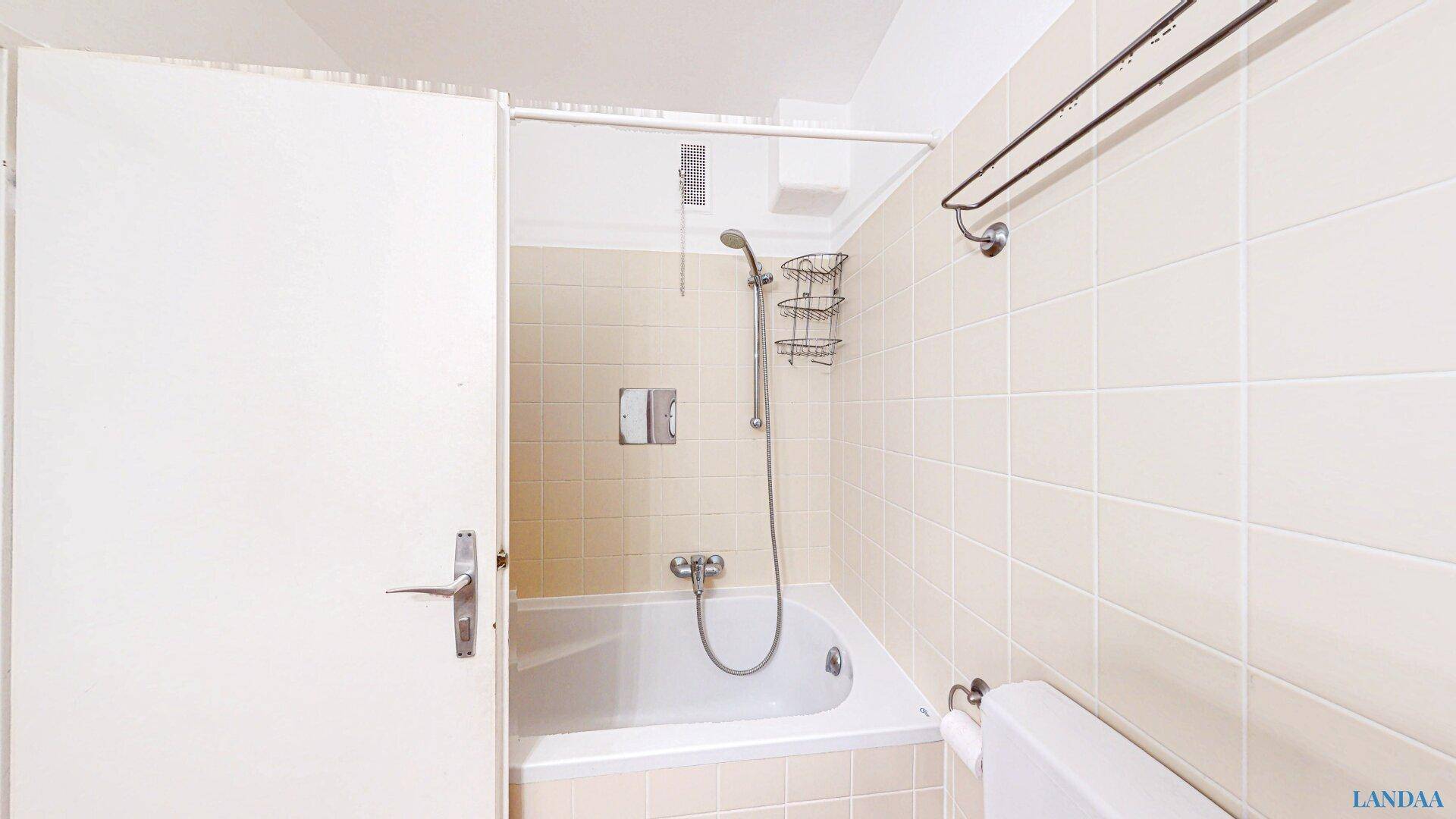 Badezimmer mit integrierter Badewanne und Duschvorrichtung, umgeben von hellen Fliesen.