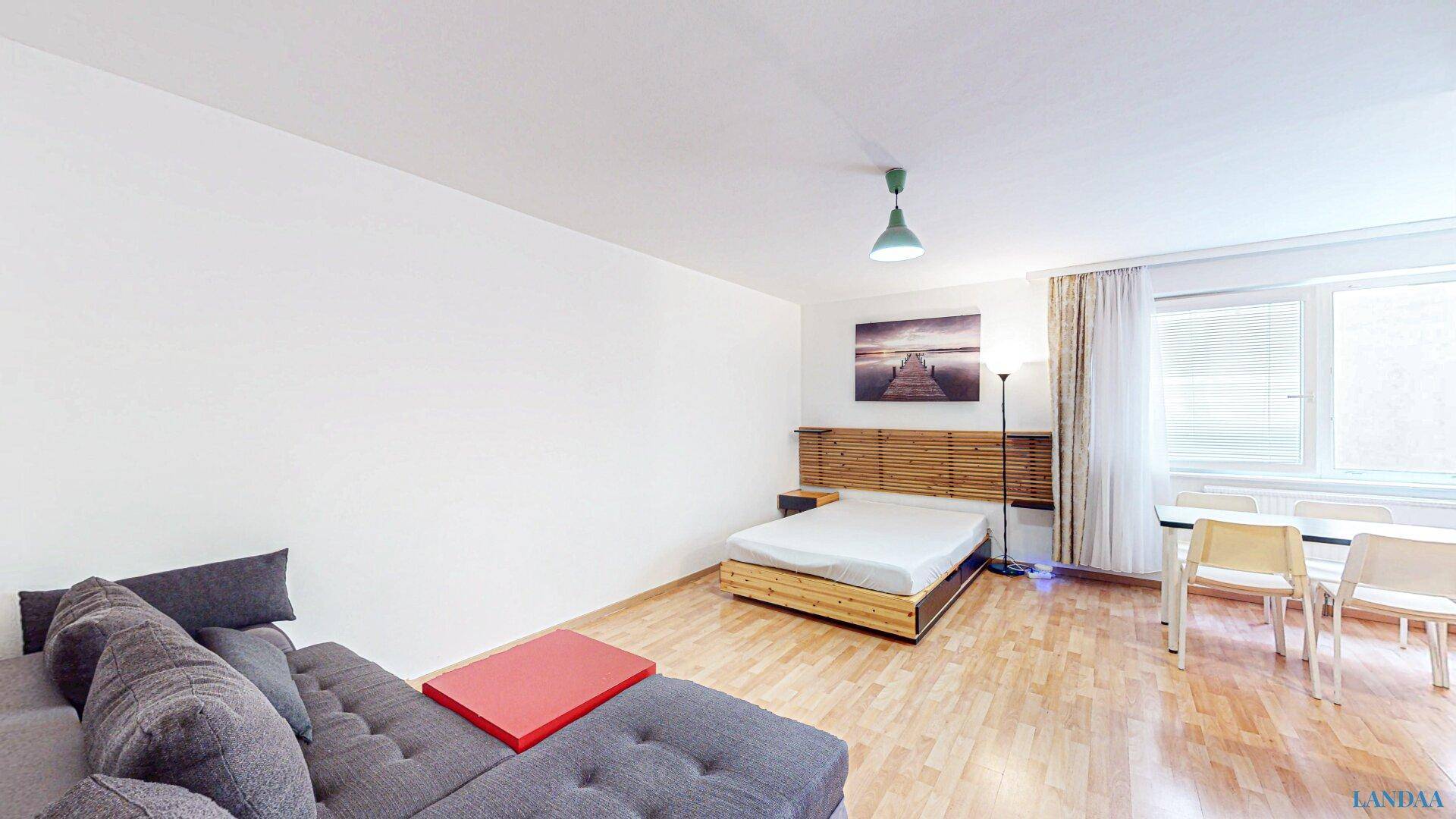 Heller Wohn- und Schlafbereich mit Sofa, Bett und Essplatz, ausgestattet mit Parkettboden.