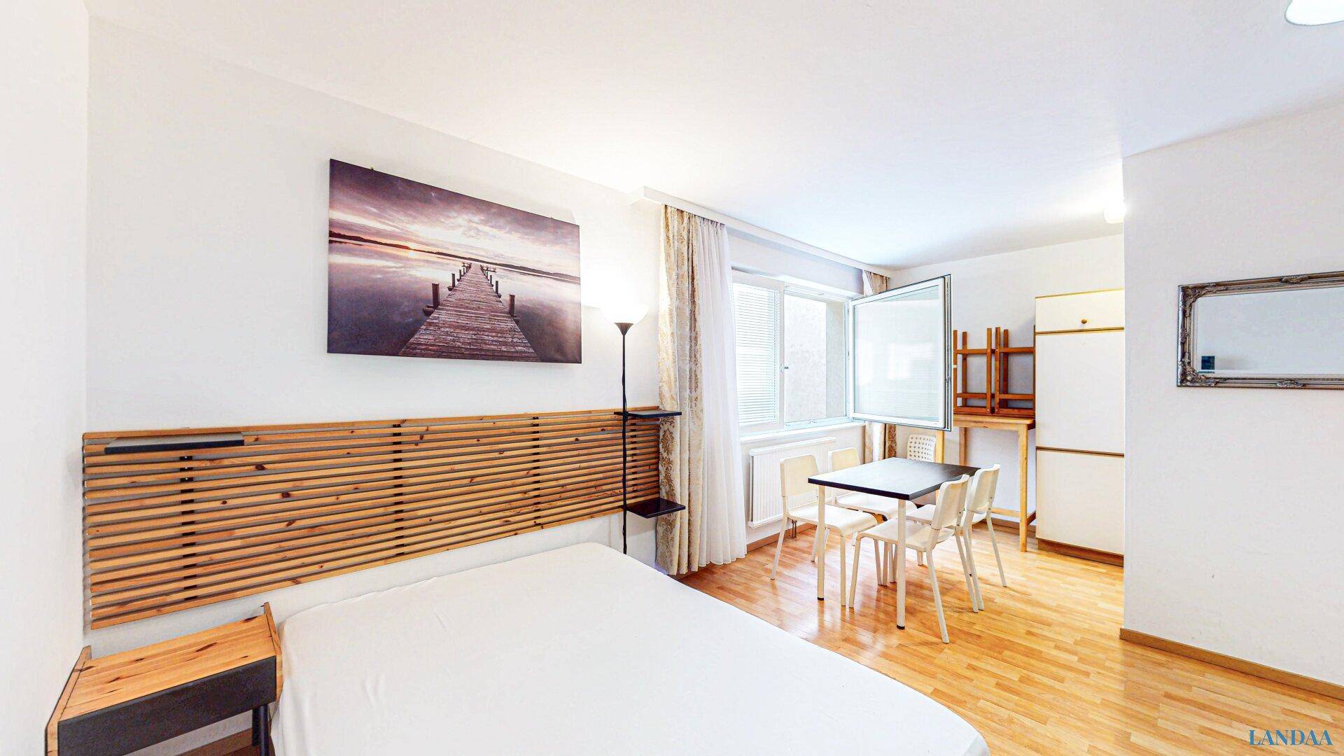 Schlaf- und Essbereich mit Holzbett, Esstisch und einem großen Fenster für viel Tageslicht.