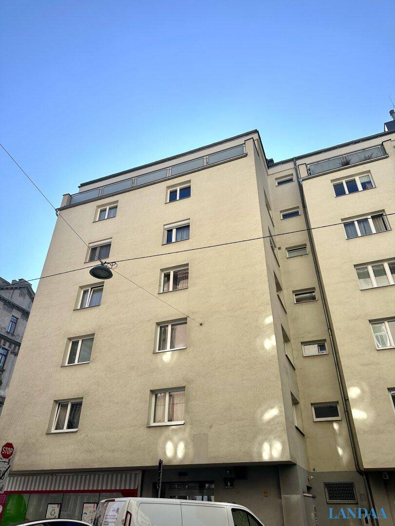 Mehrstöckiges Wohngebäude mit zahlreichen Fenstern und einer schlichten Fassade unter blauem Himmel.