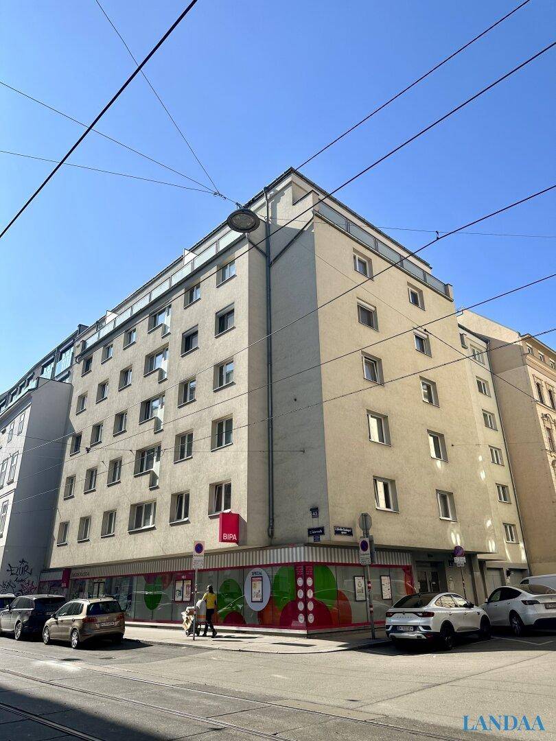 Eckgebäude mit Geschäften im Erdgeschoss und Wohnungen in den oberen Etagen, an einem sonnigen Tag.