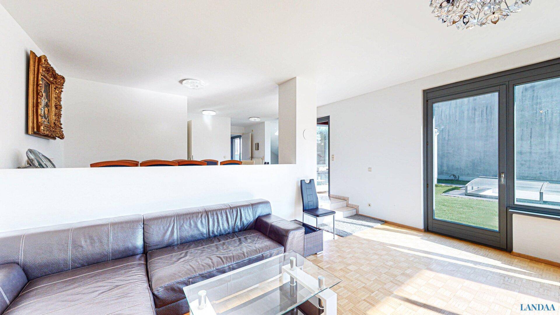 Geräumiges Wohnzimmer mit Ledersofa, Parkettboden und Zugang zum Gartenbereich.