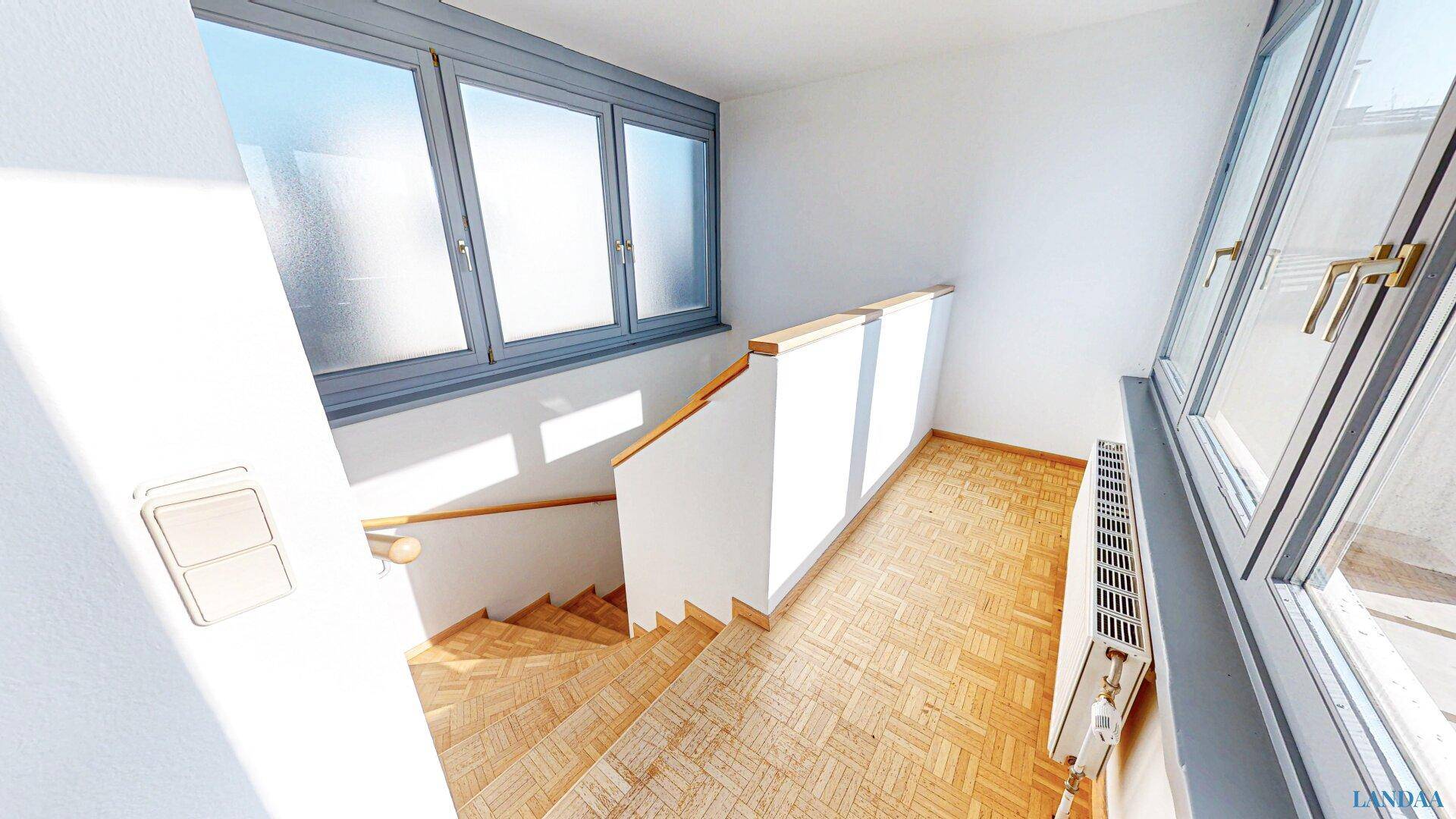 Helles Treppenhaus mit Holzstufen, Parkettboden und großen Fenstern für viel Licht.