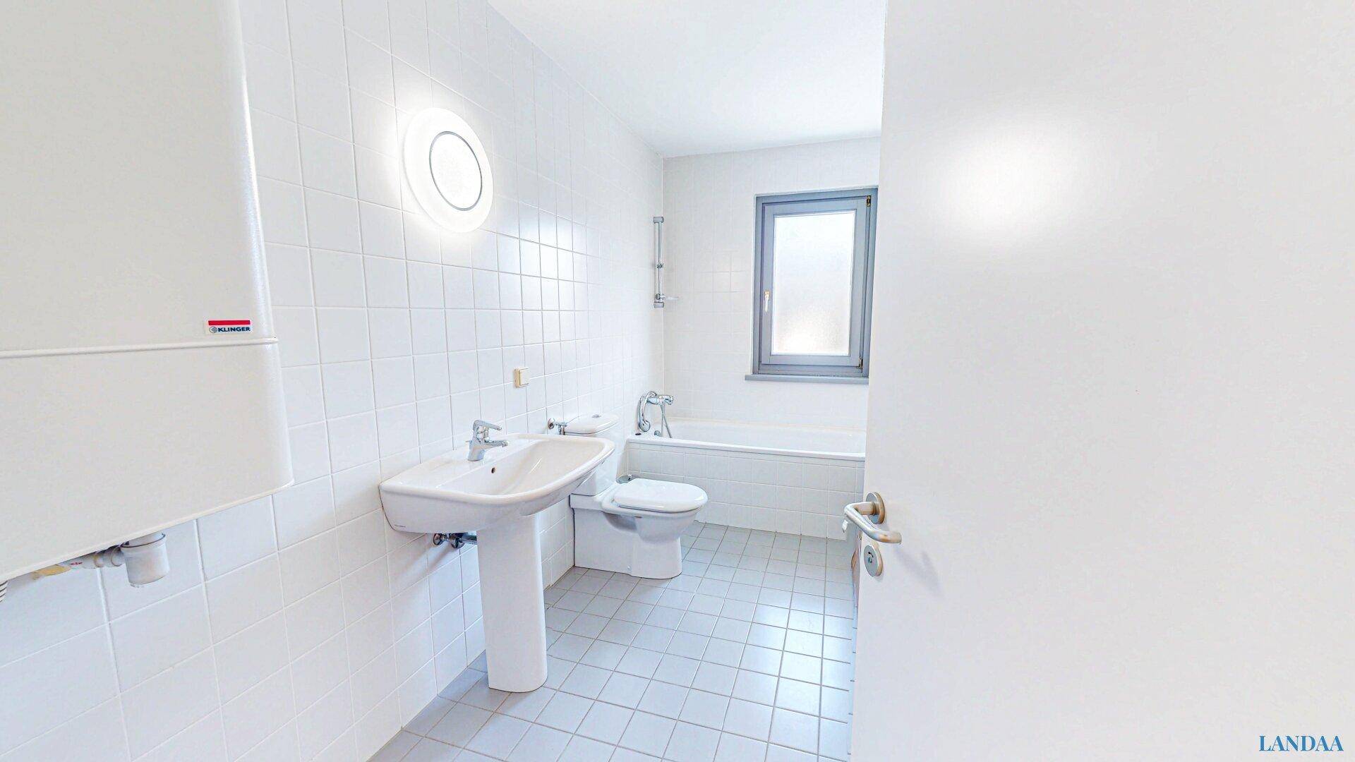 Helles Badezimmer mit Badewanne, Waschbecken und Fenster.