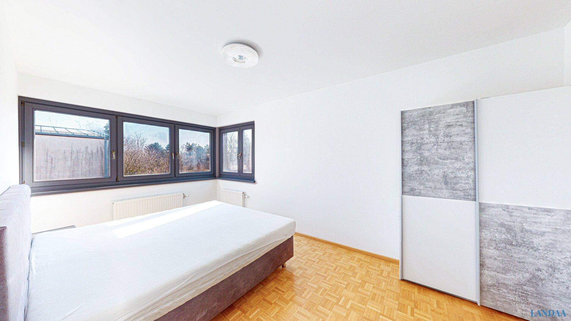 Geräumiges Schlafzimmer mit Parkettboden, großem Fenster und Kleiderschrank.