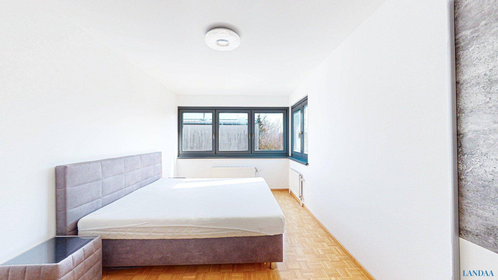 Helles Schlafzimmer mit Parkettboden, großem Fenster und modernem Bett.