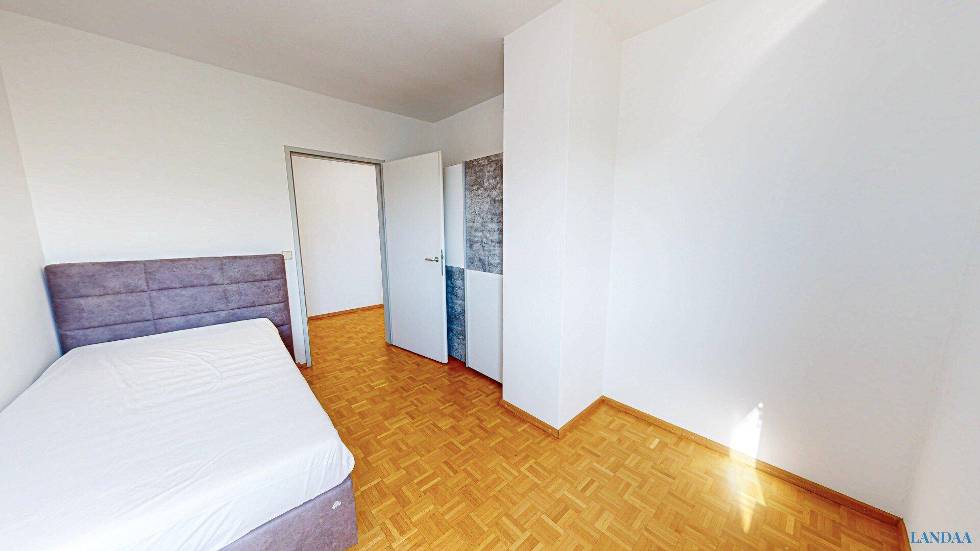 Helles Schlafzimmer mit Parkettboden, Einzelbett und Zugang zum Flur.