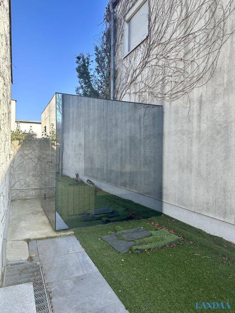 Schmaler Gartenbereich mit Rasen und einer modernen Spiegelfläche.