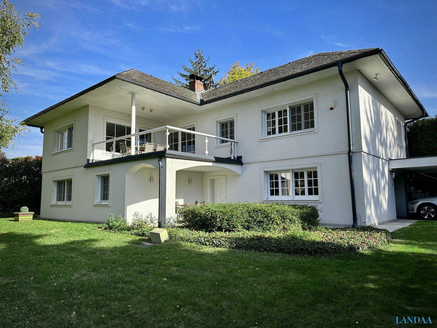 Ansicht des Hauses mit großem Garten, Balkon und Carport an einem sonnigen Tag.
