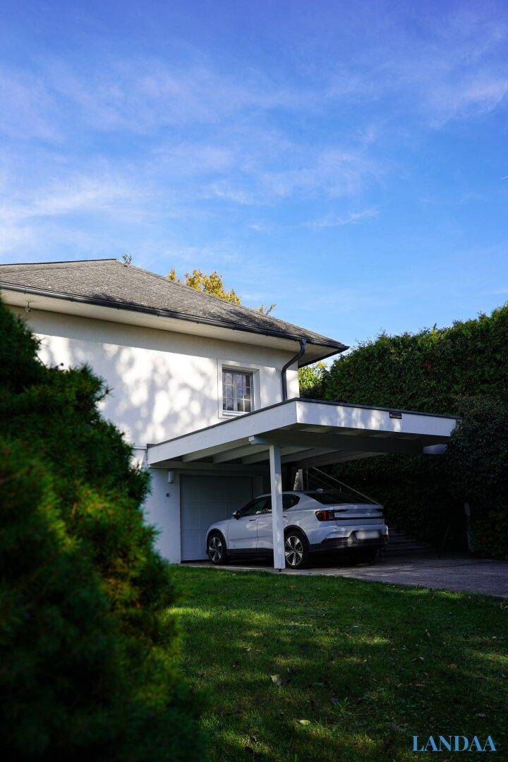 Seitenansicht des Hauses mit modernem Carport und einem gepflegten Vorgarten unter blauem Himmel.