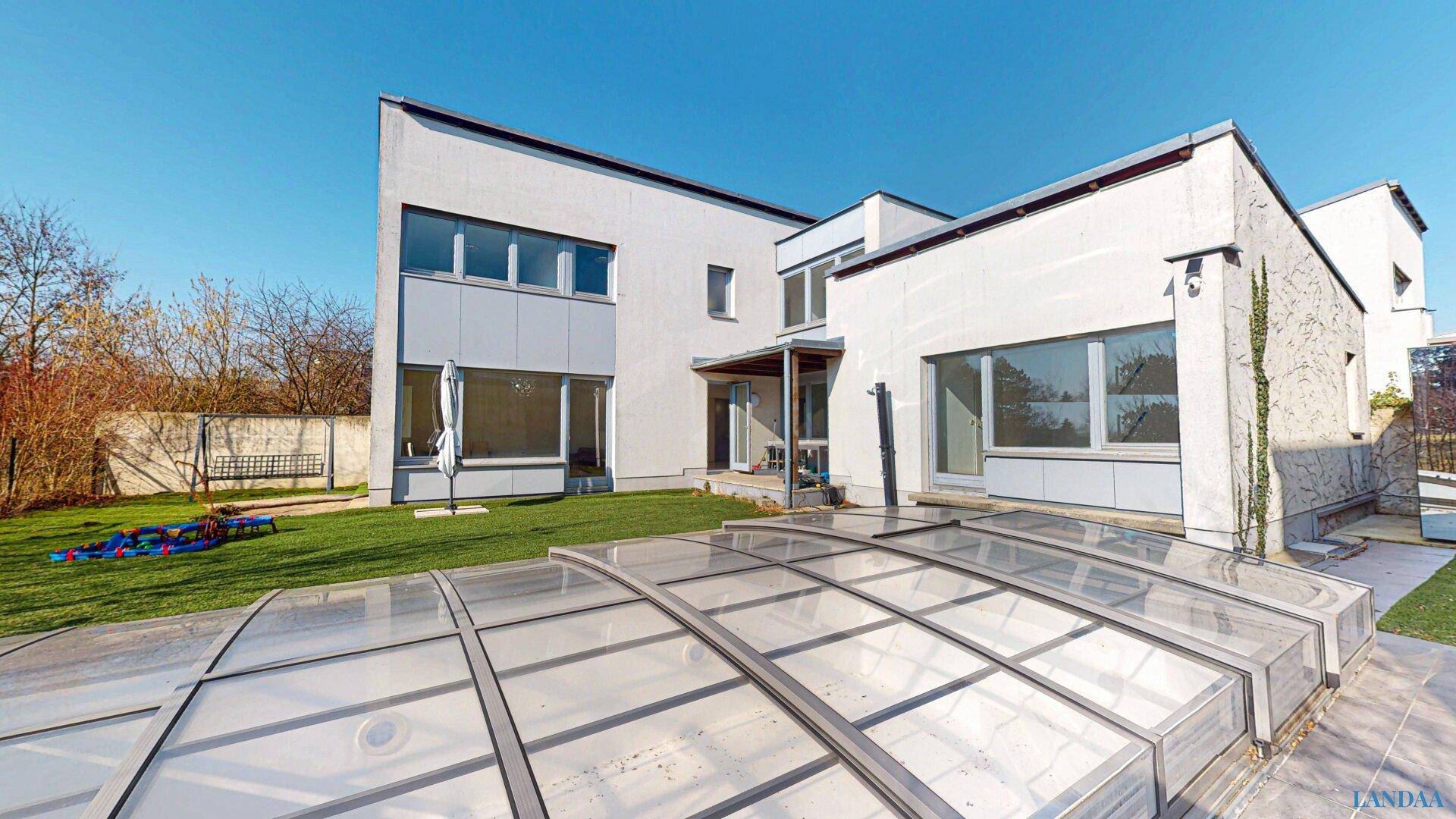 Moderne Hausfassade mit großem Garten und überdachtem Swimmingpool.