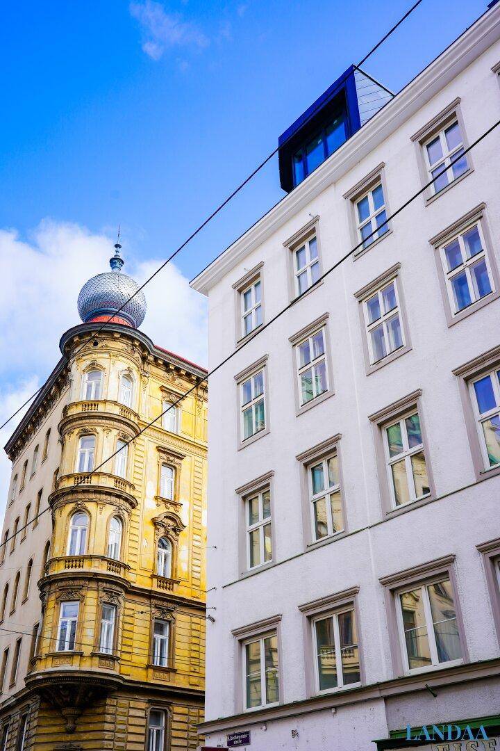 Historische Gebäude mit unterschiedlichen Fassaden und einem markanten Turm unter blauem Himmel.