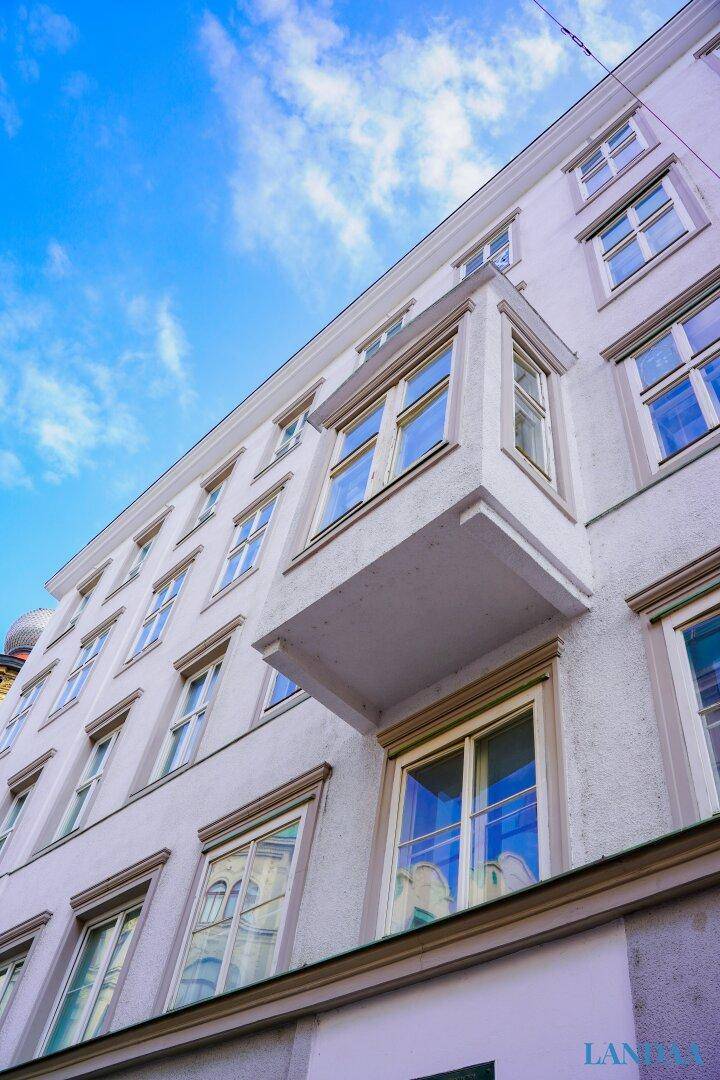 Detailansicht der weißen Fassade mit einem Erker und einem kleinen Vorsprung unter klarem Himmel.
