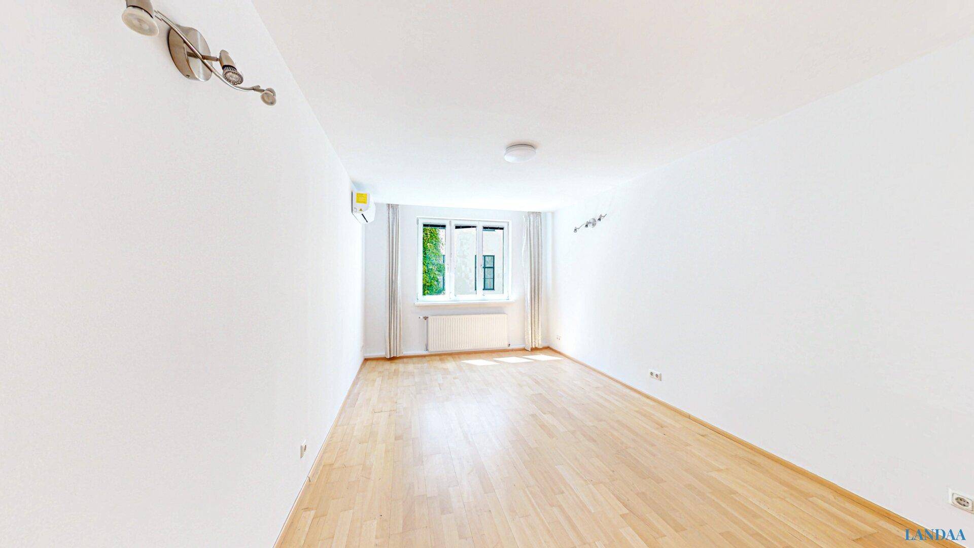 Helles, leeres Zimmer mit Holzboden, Fenster und Klimaanlage, ideal für individuelle Nutzung.