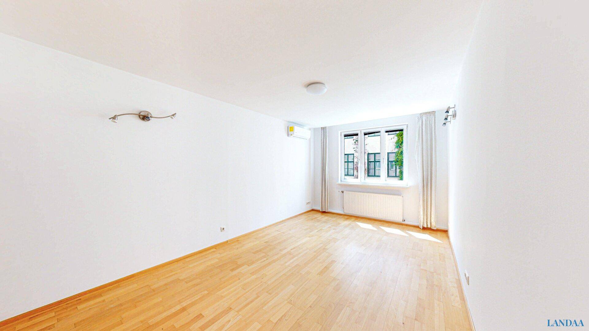 Geräumiges, helles Zimmer mit Holzboden und Fenster, bereit zur Einrichtung.