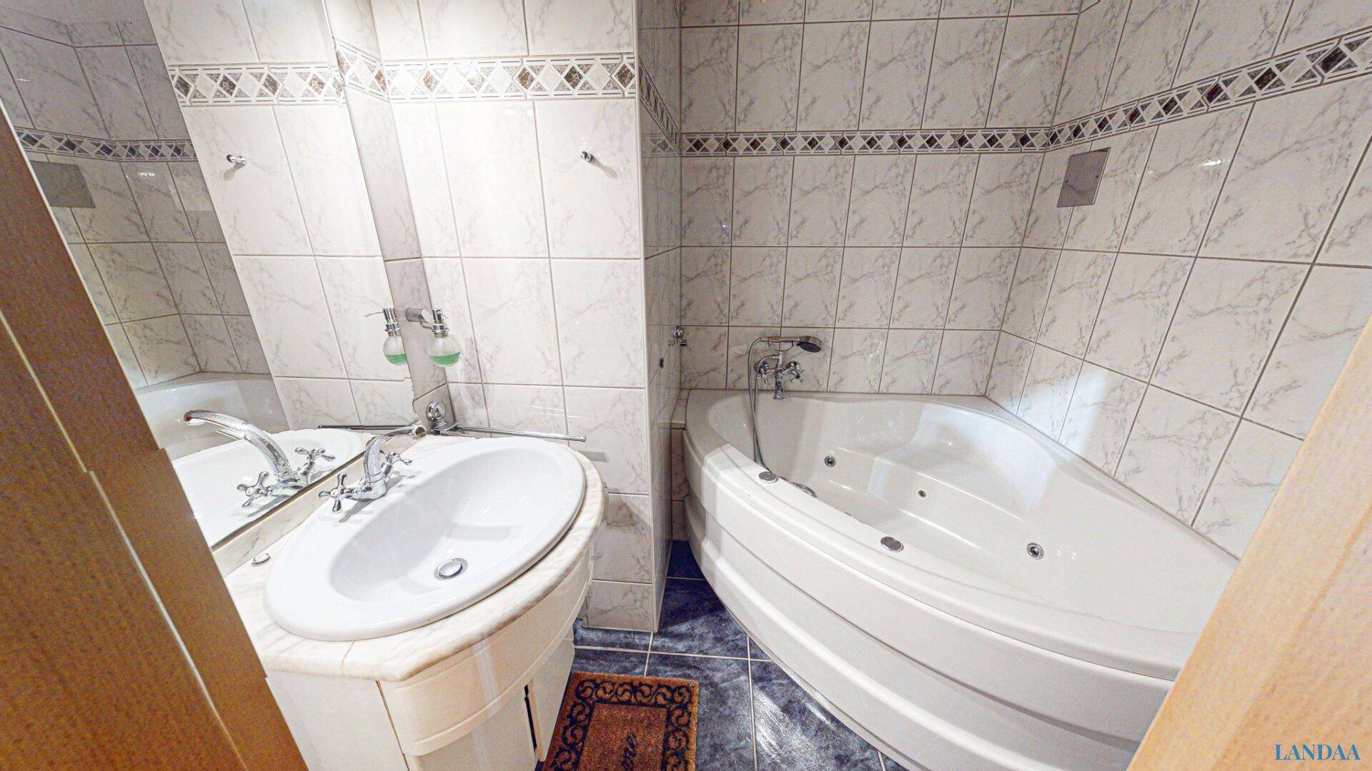 Badezimmer mit Eckbadewanne, Waschbecken und Fliesen in verschiedenen Mustern.