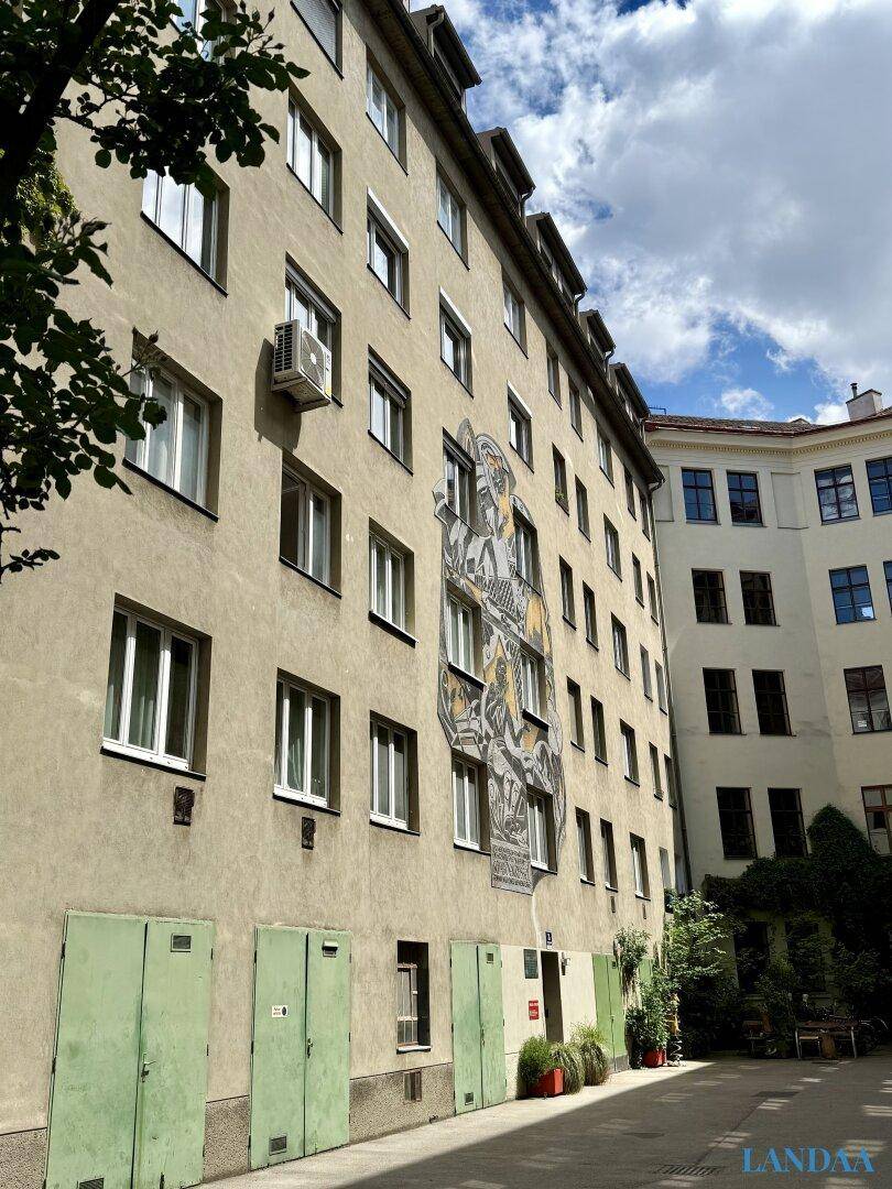 Rückseite eines Wohngebäudes mit Wandgemälde und grünen Türen im Innenhof.