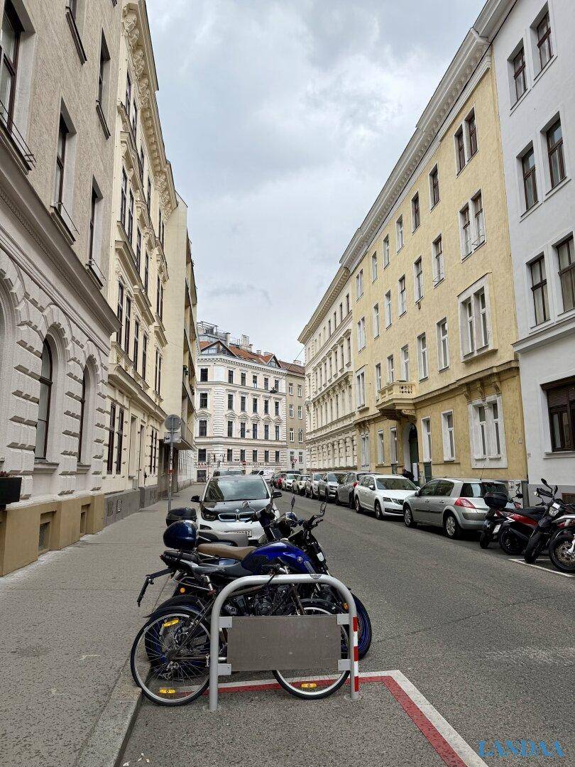 Ruhige Wohnstraße mit parkenden Autos und Fahrrädern, umgeben von Altbauten.