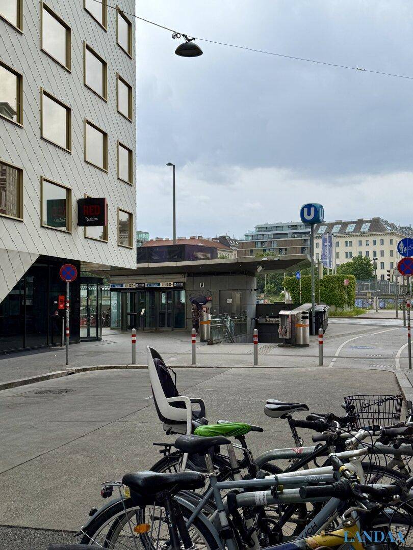 Blick auf eine moderne Gebäudefassade und eine U-Bahn-Station in urbaner Umgebung.