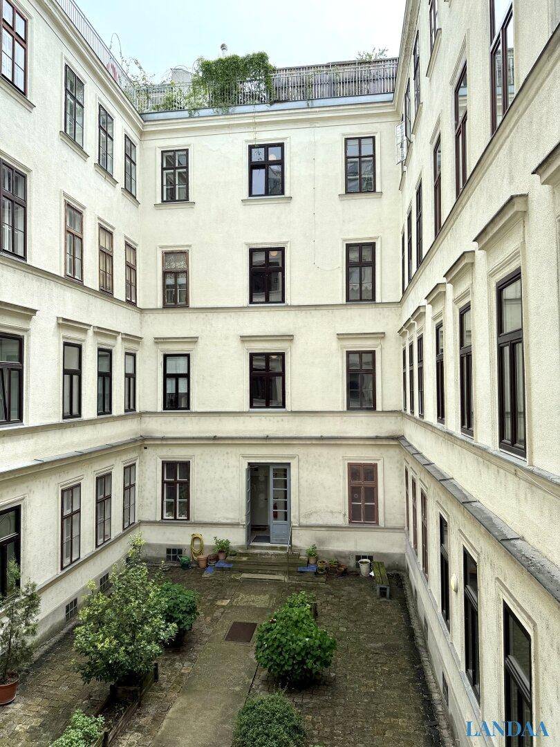 Innenhof eines Altbaus mit kleinen Bäumen und Pflanzen in Pflanzkübeln.