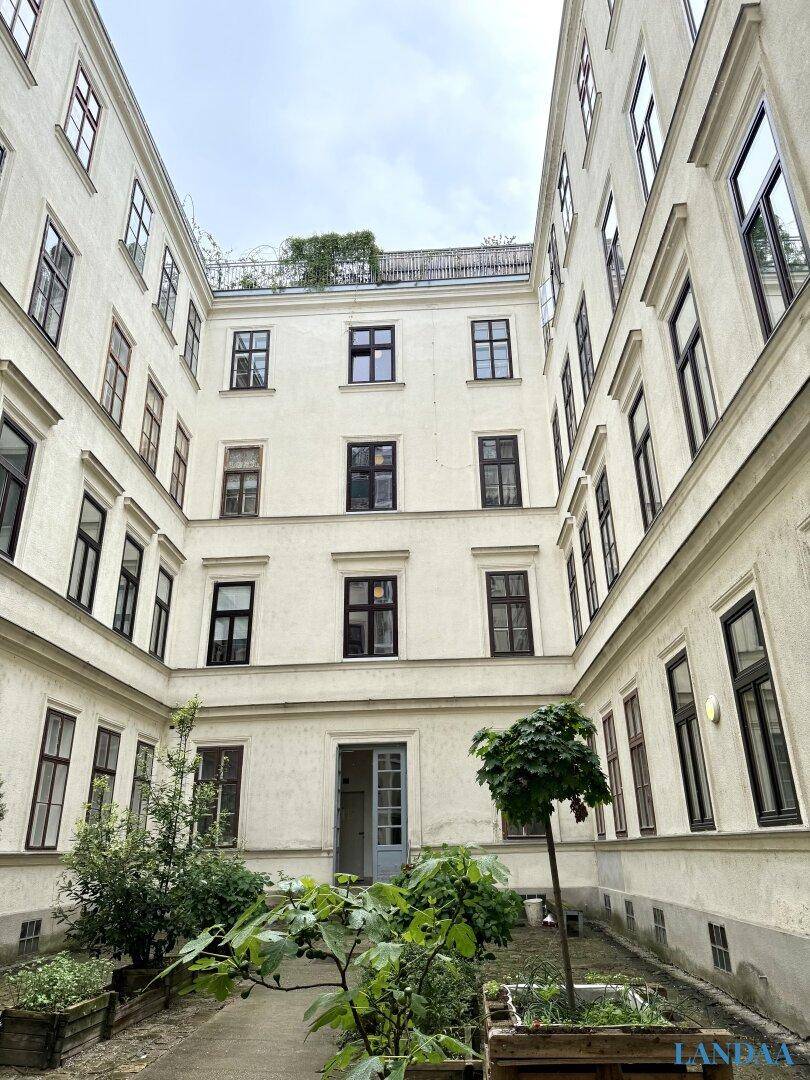 Innenhof eines Altbaus mit begrünten Beeten und vielen Fenstern.