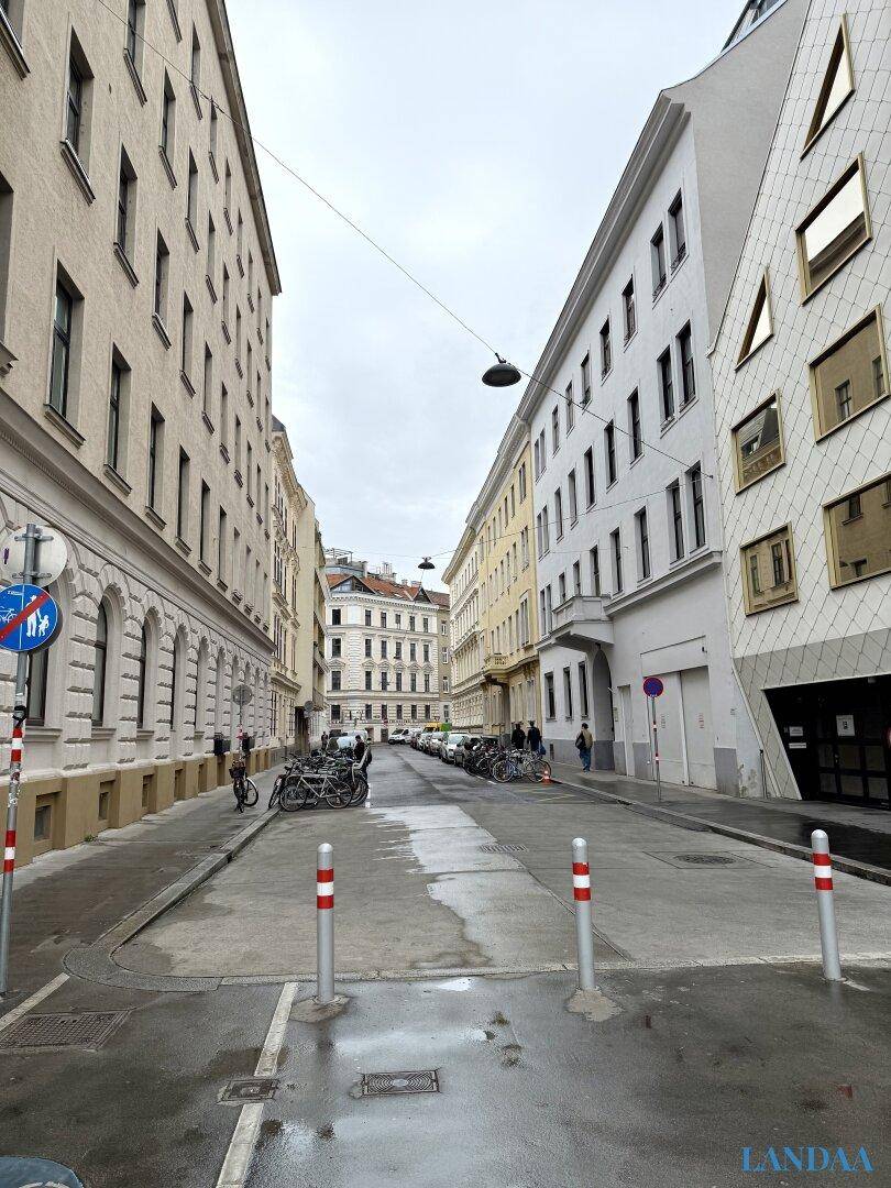 Stadtstraße mit historischen und modernen Gebäuden unter bewölktem Himmel.