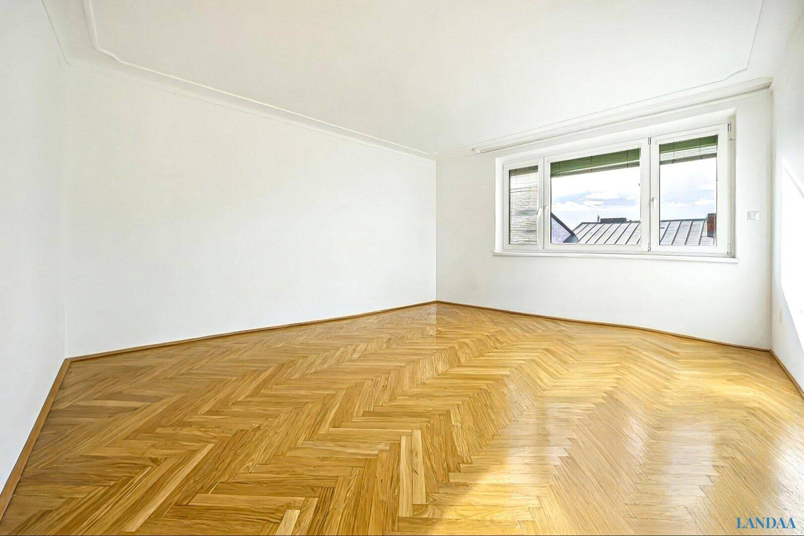 Leerer Raum mit Fischgrätparkett und Blick über die Dächer der Stadt.
