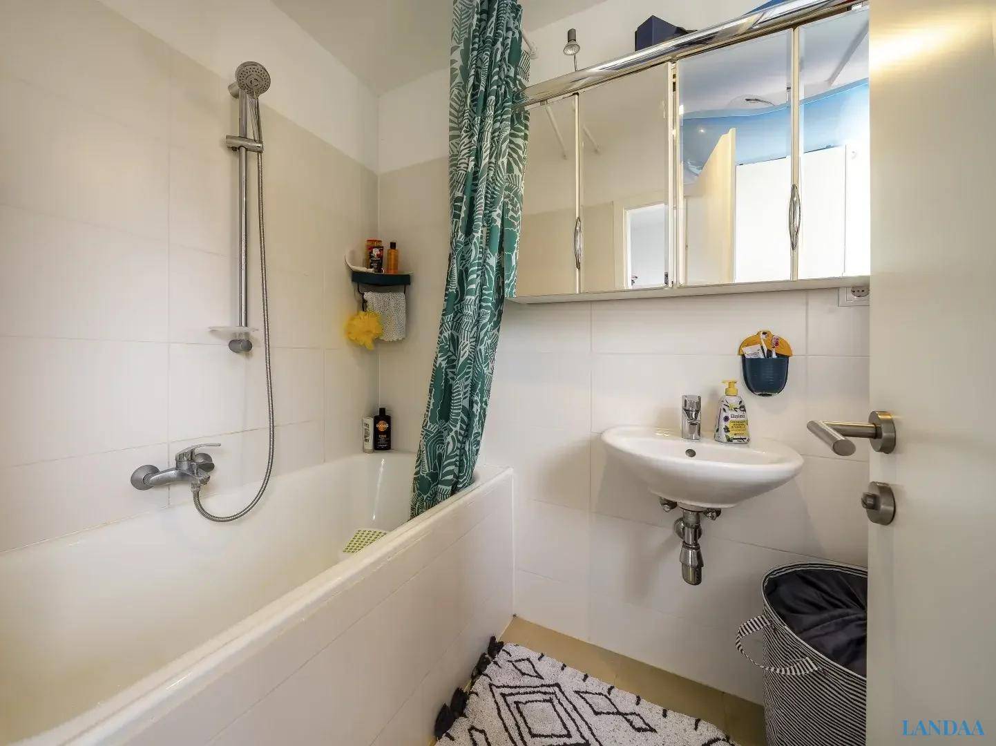 Helles Badezimmer mit Badewanne, Duschfunktion, Waschbecken und einem praktischen Spiegelschrank über dem Waschtisch.