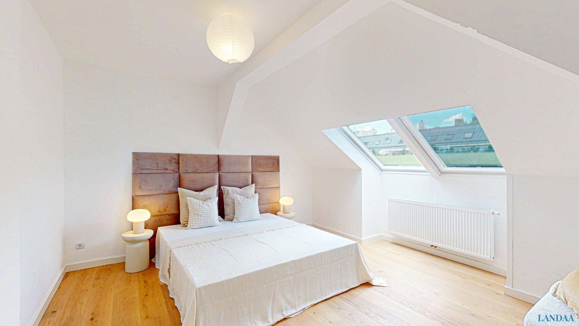 Modernes Schlafzimmer im Dachgeschoss mit großem Bett, Holzboden und zwei Dachfenstern.