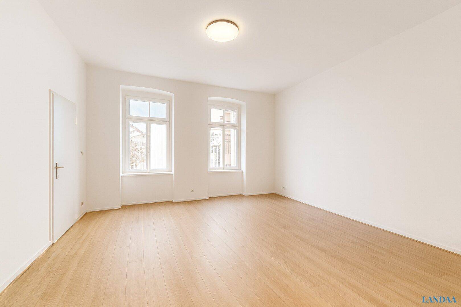Heller, leerer Raum mit Holzboden und zwei Fenstern, bereit zur individuellen Gestaltung.