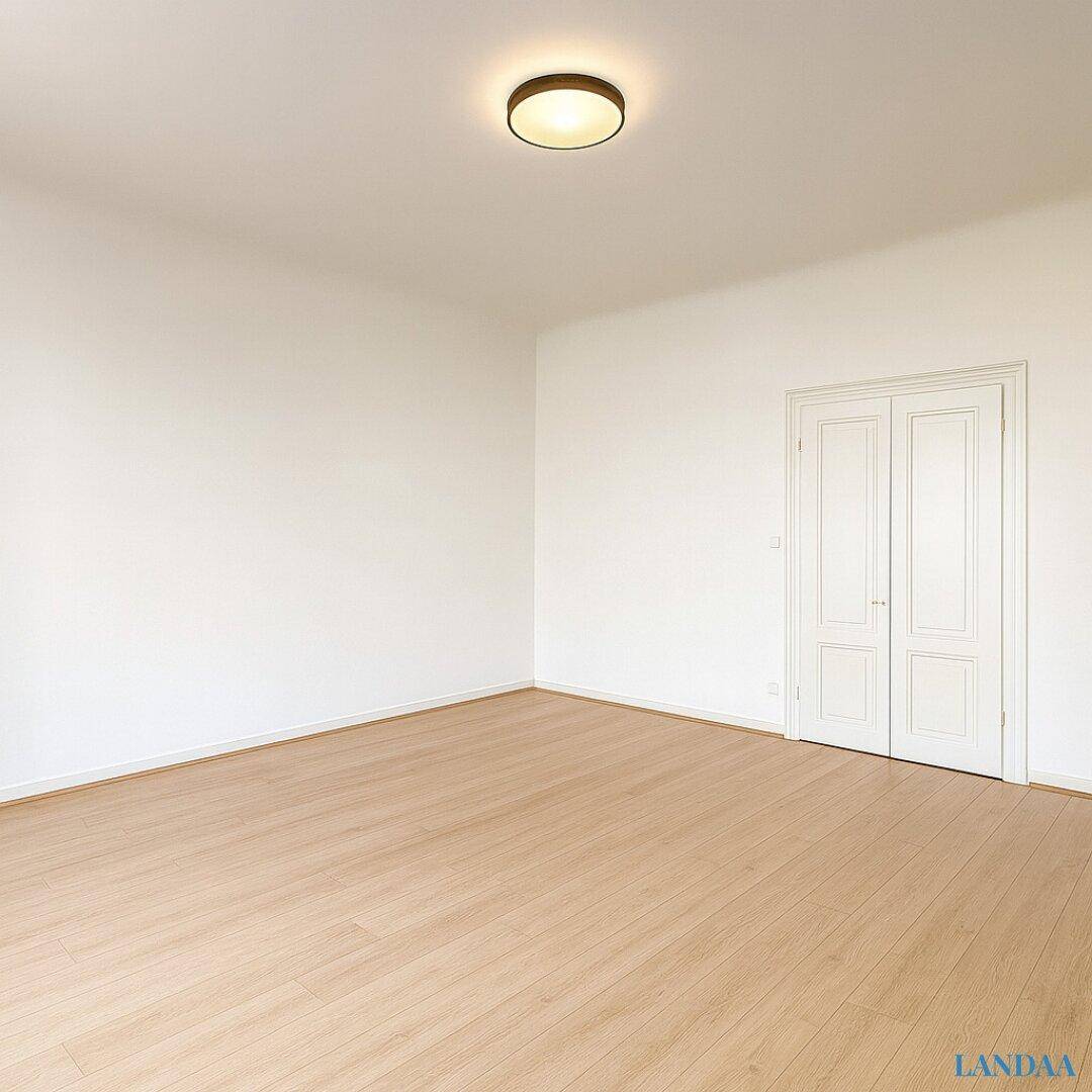 Leerer Raum mit hellem Holzboden und weißen Wänden, ausgestattet mit klassischen Doppeltüren.