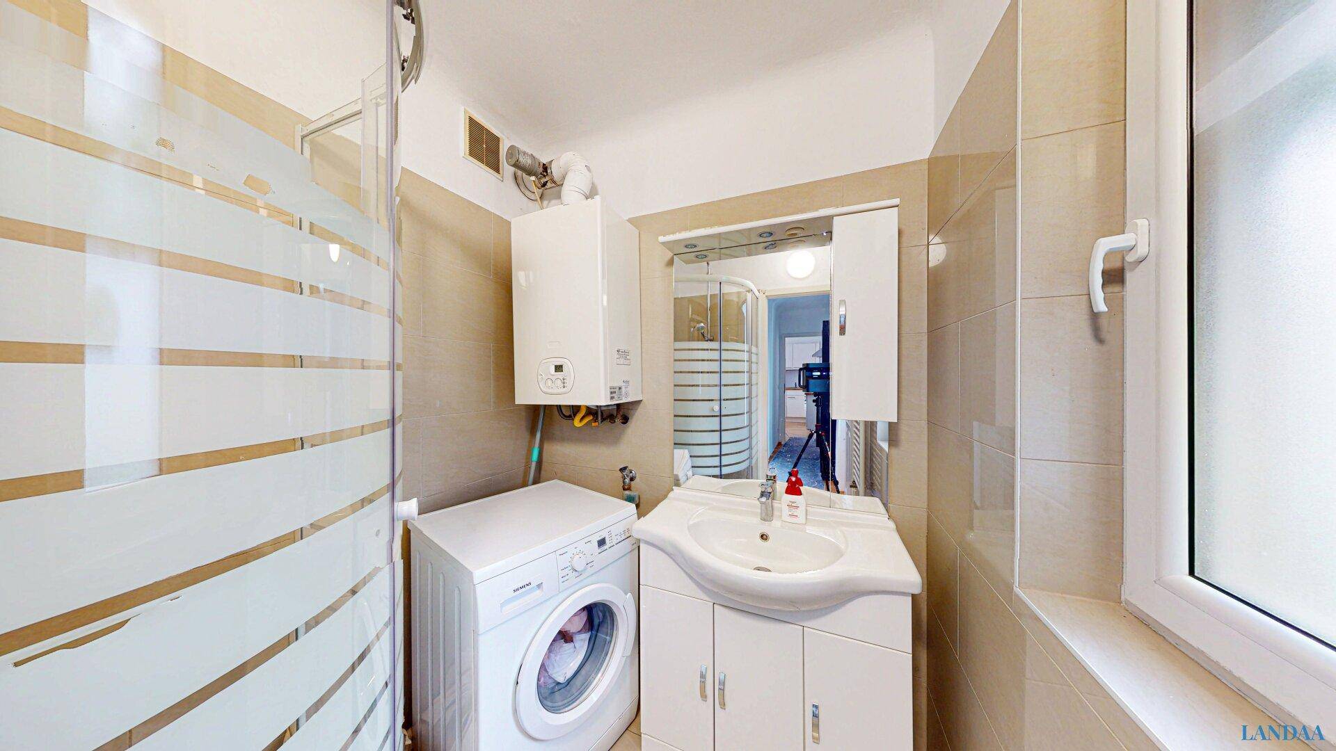 Helles Badezimmer mit Dusche, Waschbecken, Waschmaschine und Fenster für Tageslicht.