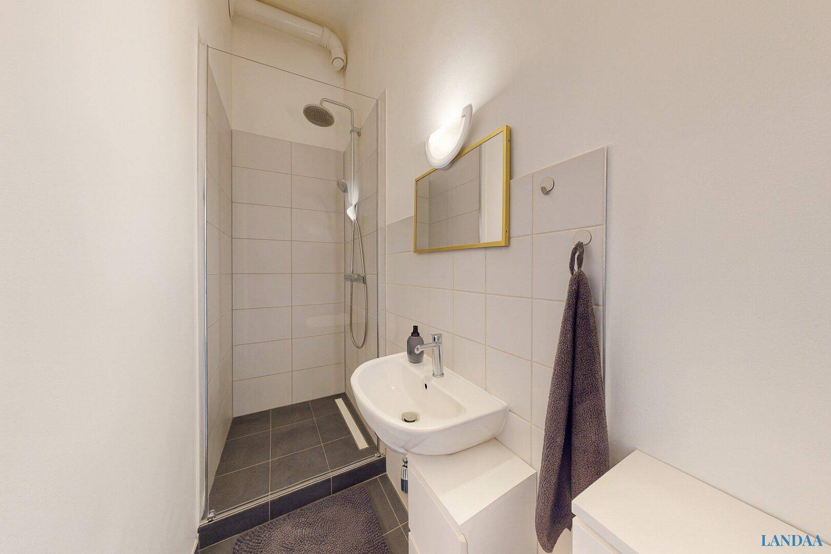 Modernes Badezimmer mit Duschkabine, Waschbecken und weißen Fliesen an den Wänden.